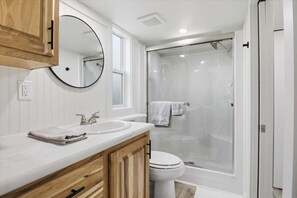 A modern bathroom with a double sink vanity, a toilet, and a glass-enclosed shower.