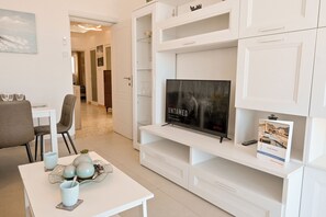 Ein modernes Wohnzimmer mit Flachbildfernseher, einem Esstisch mit Stühlen und einer weißen Vitrine.