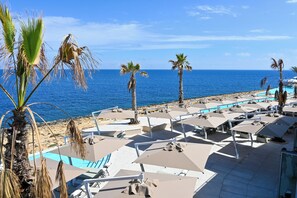 A beachside resort with sun loungers and umbrellas, a pool, and palm trees. - Exceptional Sea View Apart St Paul's Bay, Saint Paul's Bay, Malta (Saint Paul's Bay)