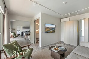 Ein modernes Hotelzimmer mit einer Sitzecke, einem Couchtisch, einem Essbereich und einer Küche im Hintergrund.