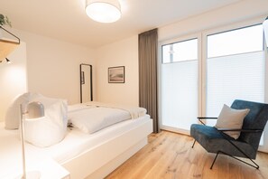 Ein modernes Schlafzimmer mit Bett, Stuhl, Nachttisch und einem Fenster mit Jalousien.
