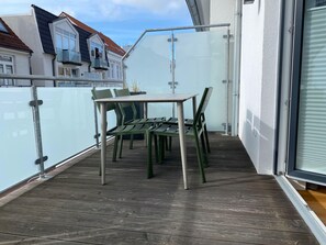 Ein Balkon mit Tisch und Stühlen, einer Glasufernung und Blick auf benachbarte Häuser.