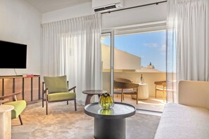 A modern hotel room with a flat-screen TV, a sofa, a chair, a small table, and a balcony with outdoor furniture. - Domaine De Cocagne N°3 - Pool & Sea View, Cagnes sur Mer, France (Cagnes sur Mer)