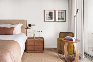 Ein modernes Hotelzimmer mit Bett, Nachttisch, Lampe, Sessel und zwei gerahmten Bildern an der Wand.