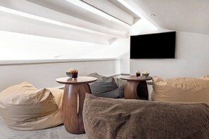 A modern living room with a high ceiling, two round wooden tables, a flat-screen TV mounted on the wall, and a sofa with multiple cushions. - Domaine De Cocagne N°3 - Pool & Sea View, Cagnes sur Mer, France (Cagnes sur Mer)