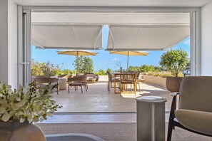 Eine Terrasse im Freien mit Tisch, Stühlen und zwei Sonnenschirmen, mit Blick auf die umliegende Landschaft.