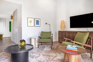 Ein modernes Wohnzimmer mit Flachbildfernseher, zwei grünen Sesseln, einem Couchtisch und einer Stehlampe.