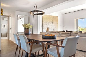 Uma área de jantar moderna com mesa de madeira, cadeiras claras, um vaso com flores e uma tigela de laranjas.