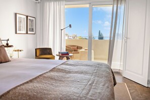Quarto de hotel com uma cama grande, uma cadeira, uma mesa pequena e varanda com vista.