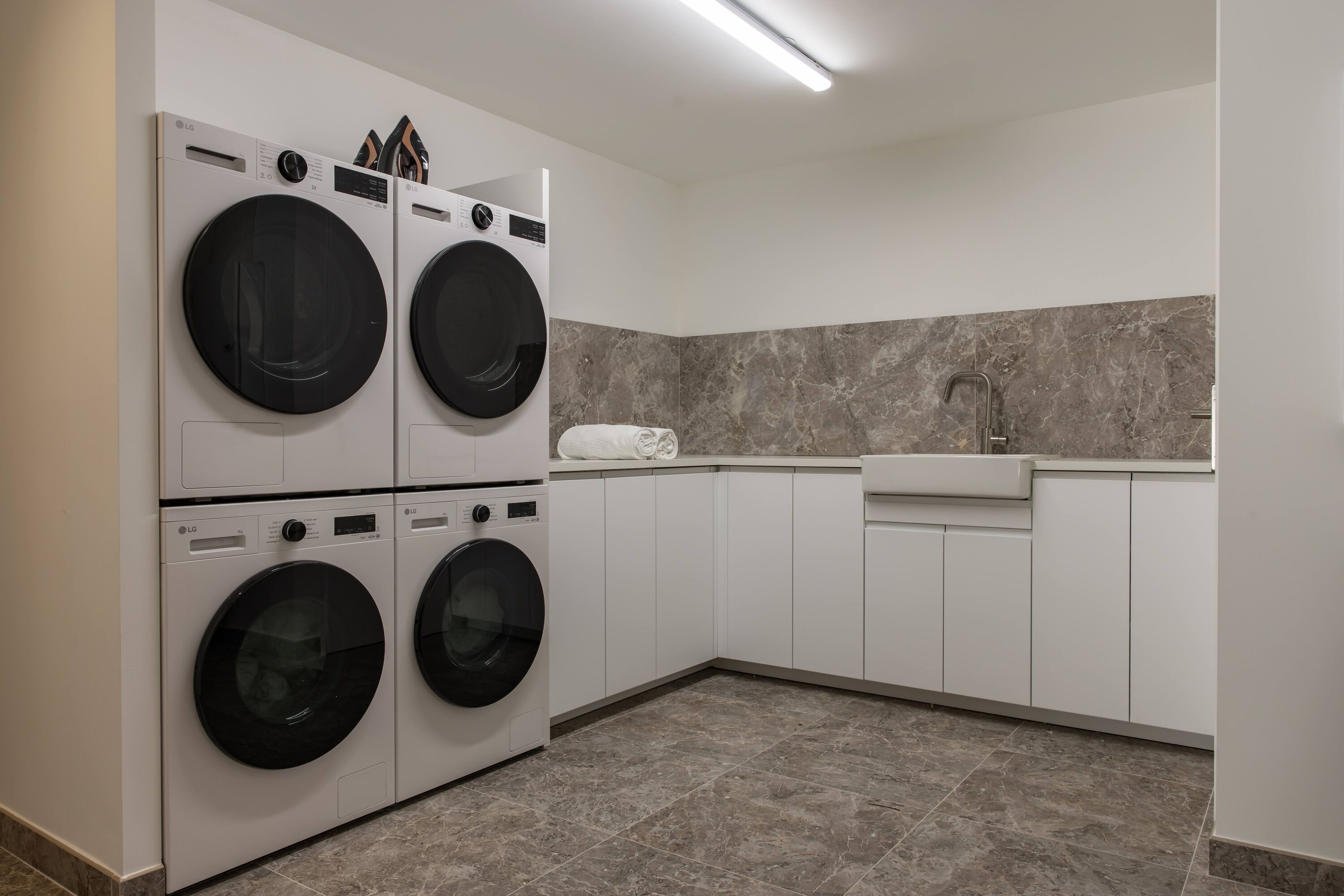A laundry room with four LG washing machines, a sink, and a marble-tiled backsplash.