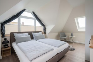 Ein Schlafzimmer mit schrägem Dach, einem Bett, einem Sessel, einem kleinen Tisch und einem Fenster.