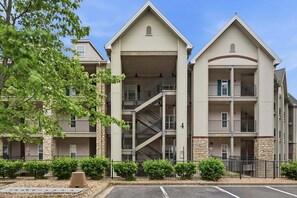 A multi-story building with a central staircase, balconies, and a parking lot. - Branson Condo with Golf Course View • 3 King Suites • Sleeps 6 (Branson)