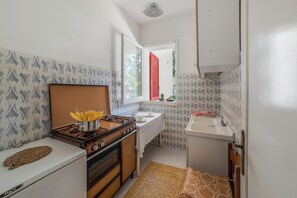 Eine kleine Küche mit einem Gasherd, einem Kühlschrank, einer Spüle und einem Fenster mit roten Fensterläden.