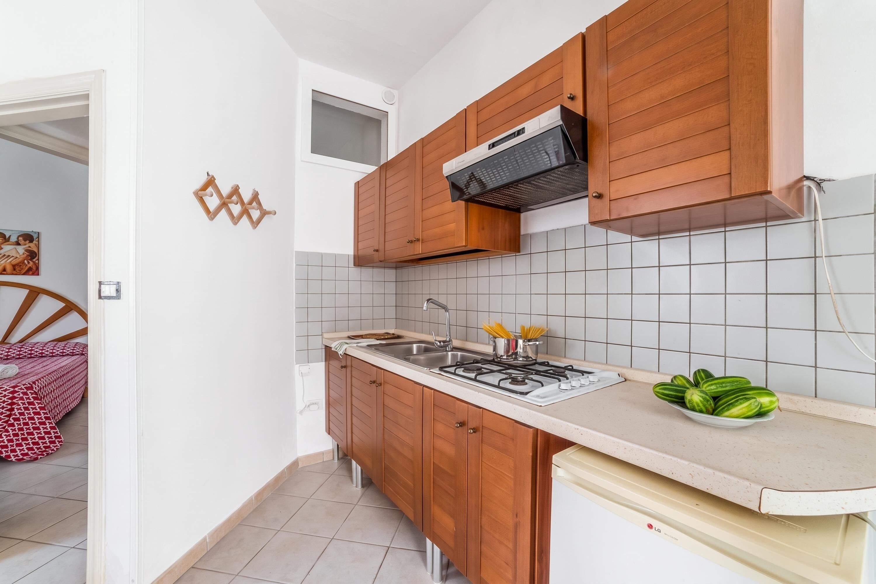 Een kleine keuken met houten kastjes, een gasfornuis en een betegelde spatwand.