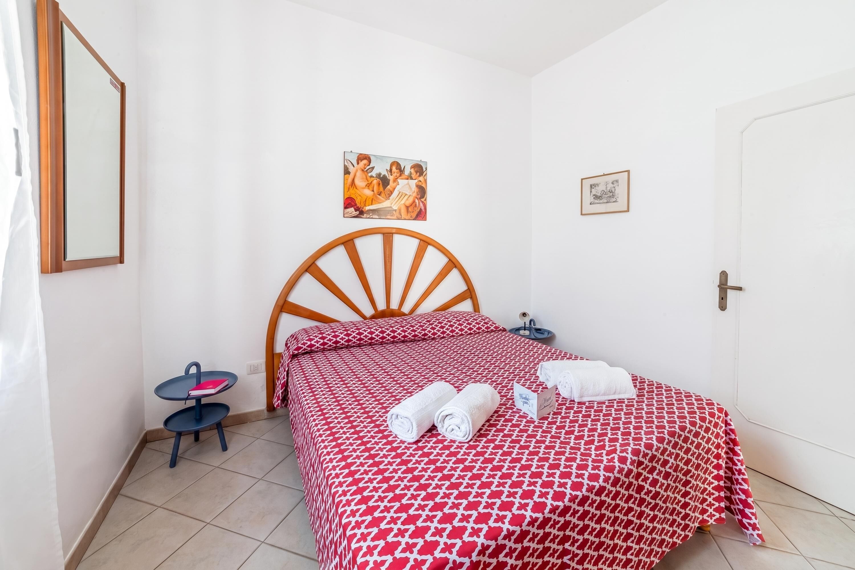 Un dormitorio con cama de madera, una mesita de noche pequeña, una silla y un cuadro colgado en la pared.