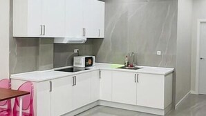 A modern kitchen with white cabinets, a microwave, and a pink chair. - Hostal Casa 18 (Madrid)