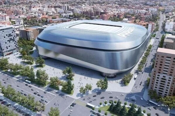 A modern, curved building with a flat roof, surrounded by a cityscape and greenery. - Hostal Casa 18 (Madrid)