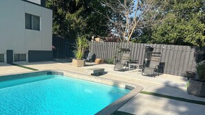 A rectangular swimming pool with a tiled edge, surrounded by a concrete patio with a small grassy area. -     The Pinery | Modern Retreat with Pool & Family-Friendly Comfort (St. Catharines)
