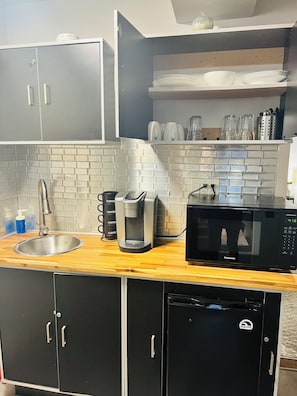 A kitchen with a sink, coffee maker, microwave, cabinets, and a tiled backsplash.