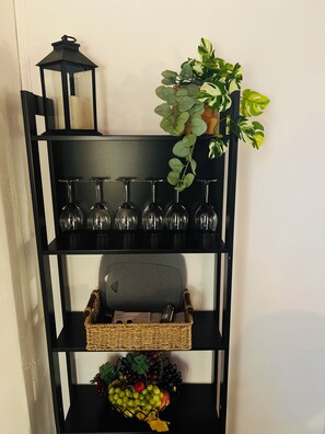 A black metal shelf with wine glasses, a lantern, a plant, and a basket of fruit.