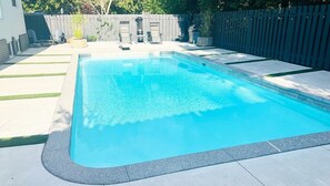 Piscina retangular com borda escura, rodeada por um deck de concreto e uma cerca de madeira.