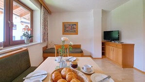 Ein Essbereich mit einem Tisch für zwei Personen, einem Fernseher und einem Fenster mit Vorhängen.