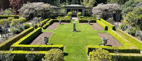 A formal garden with geometrically trimmed hedges, a central pavilion, and stone urns.