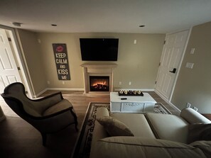 A living room with a fireplace, a television mounted above it, a sofa, and a chair. - Stay on Beautiful Glen Lake Victoria (Victoria)