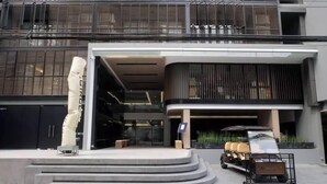 Un edificio moderno con una entrada curva, una escultura y un vehículo estacionado afuera.