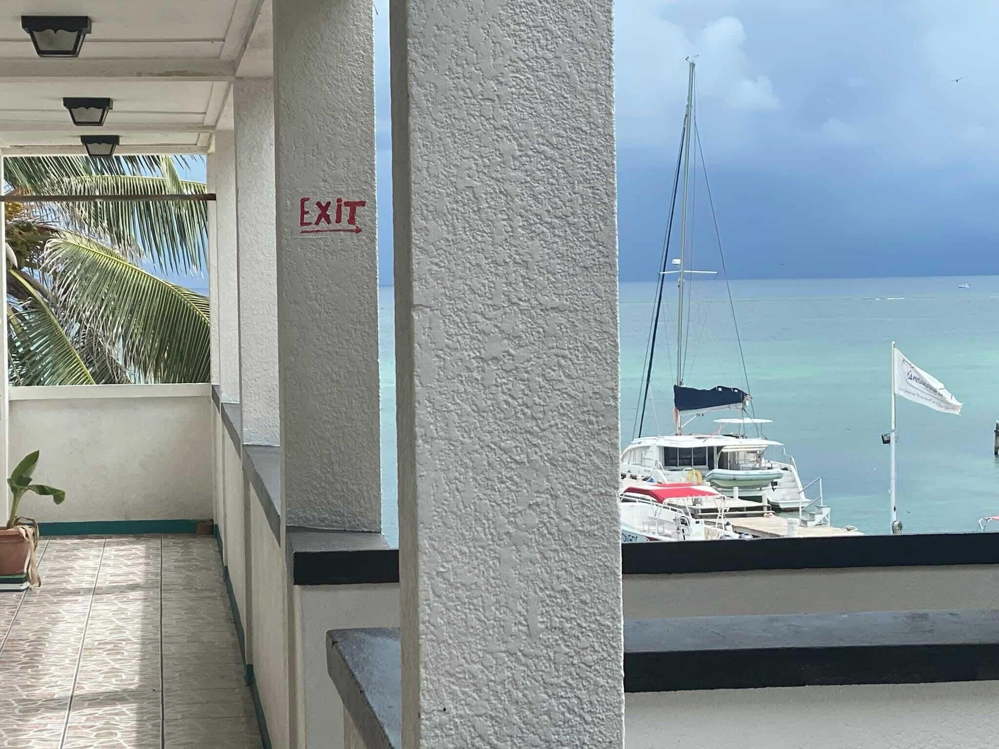 A balcony with a view of the sea, a potted plant, and an exit sign.