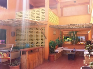 A covered outdoor area with a grill, seating, and potted plants.
