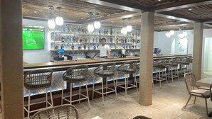 A bar area with a bartender, wicker chairs, and a shelf with bottles.
