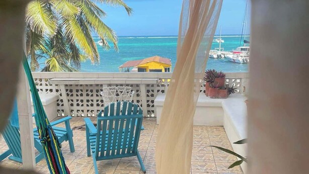 A balcony with a view of the ocean, a hammock, and blue chairs.