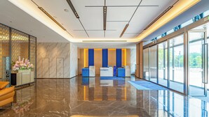 Um hall moderno com piso de mármore, balcão de recepção e grandes janelas com vista para o exterior.
