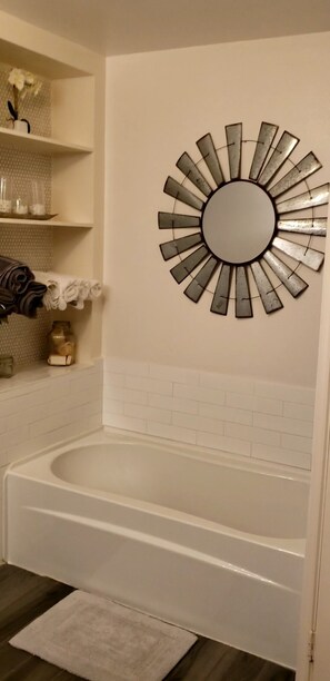 Ein Badezimmer mit einer weißen Badewanne, einem runden Spiegel mit Sonnendesign und einem Ablagefach für Toilettenartikel.