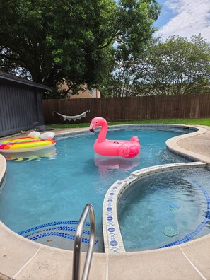 Ein Swimmingpool mit einem rosa Flamingo-Schwimmding, einem Regenbogen-Schwimmding und einer Hot-Tub mit blauen Mosaikfliesen.
