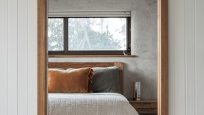A bedroom with a bed, pillows, a bedside table, a nightstand, a window, and a wall-mounted light fixture.