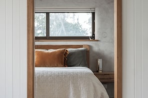 A bedroom with a bed, pillows, a bedside table, a nightstand, a window, and a wall-mounted light fixture. - A unique, luxurious, eco-friendly hempcrete home on Bruny Island. Pet friendly! (Alonnah)