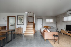 A modern living space with a staircase, a sofa, a TV, and a dining area.