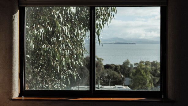 A window with a view of a body of water, trees, and distant landforms.