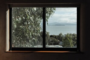 A window with a view of a body of water, trees, and distant landforms.