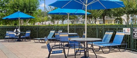 Outdoor seating with blue umbrellas, a round table, and lounge chairs.