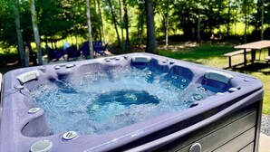 Ein Whirlpool inmitten von Bäumen, mit Stühlen und einem Picknicktisch im Hintergrund.