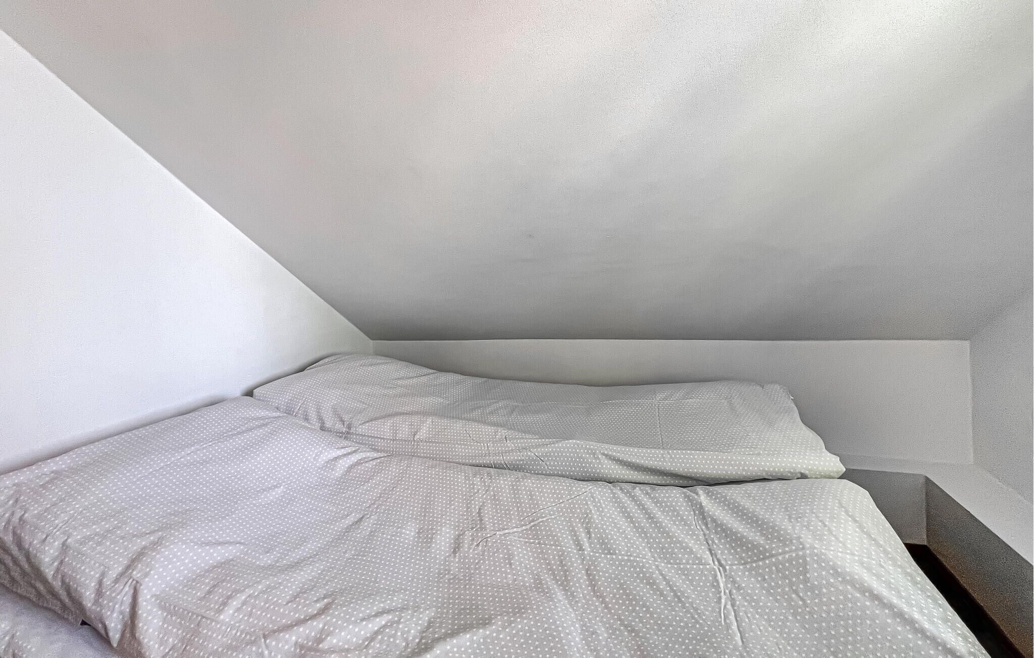 Ein kleines Zimmer mit einem Einzelbett, schräg gedachter Decke und schlichten Wänden.