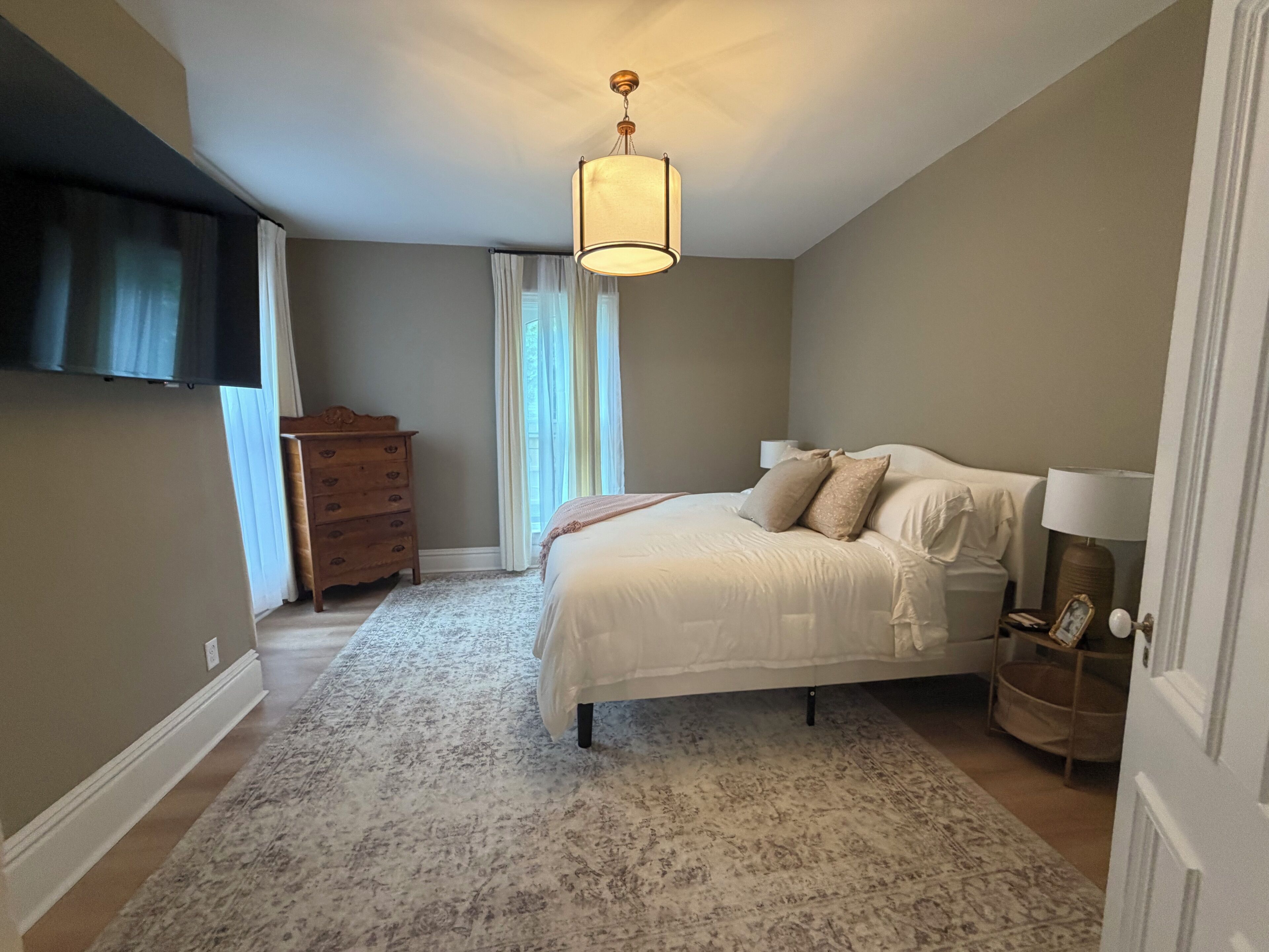 A bedroom with a bed, a dresser, a nightstand, a lamp, and a ceiling light.