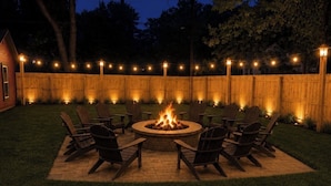 A circular outdoor seating area with chairs around a central fire pit, surrounded by a wooden fence and string lights. - Victorian home 7-bedroom homes with full mother on law suite in back (La Porte)
