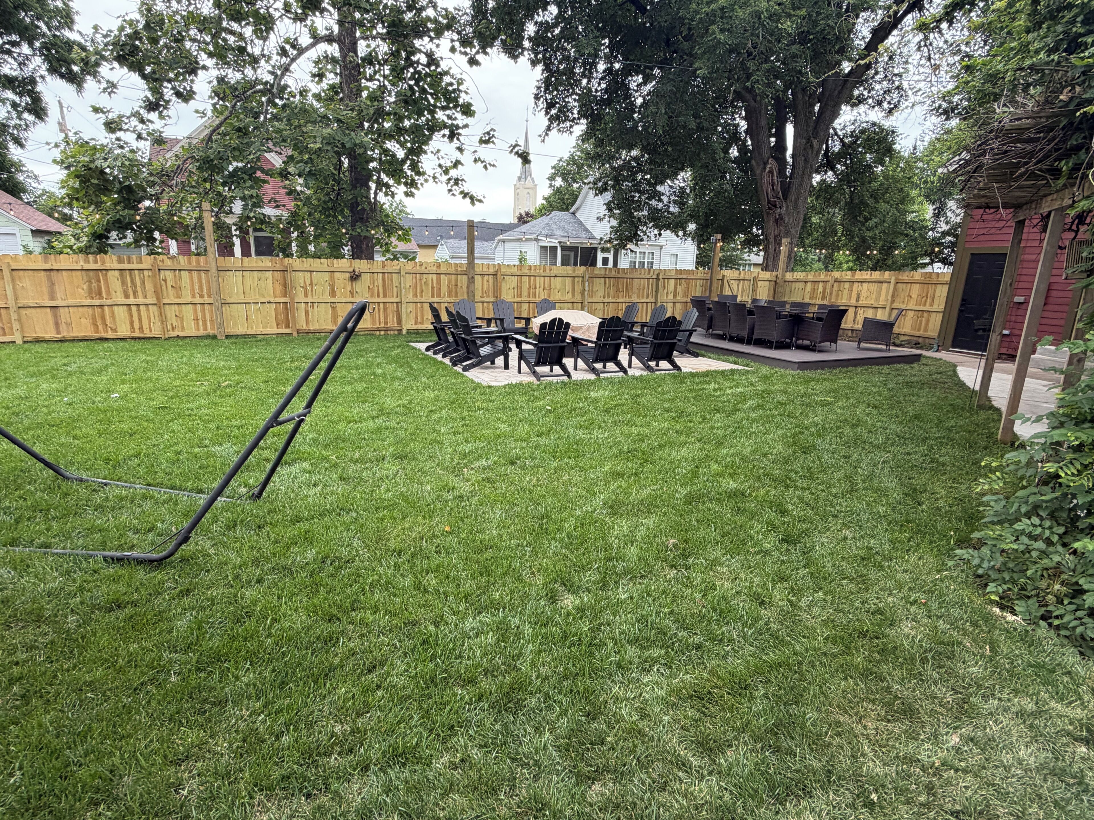 A backyard with a lawn, a wooden fence, and a patio area with chairs and tables.