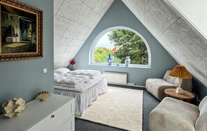 Een slaapkamer met een bed, een kaptafel, een raam met uitzicht op bomen, en een schilderij aan de muur.