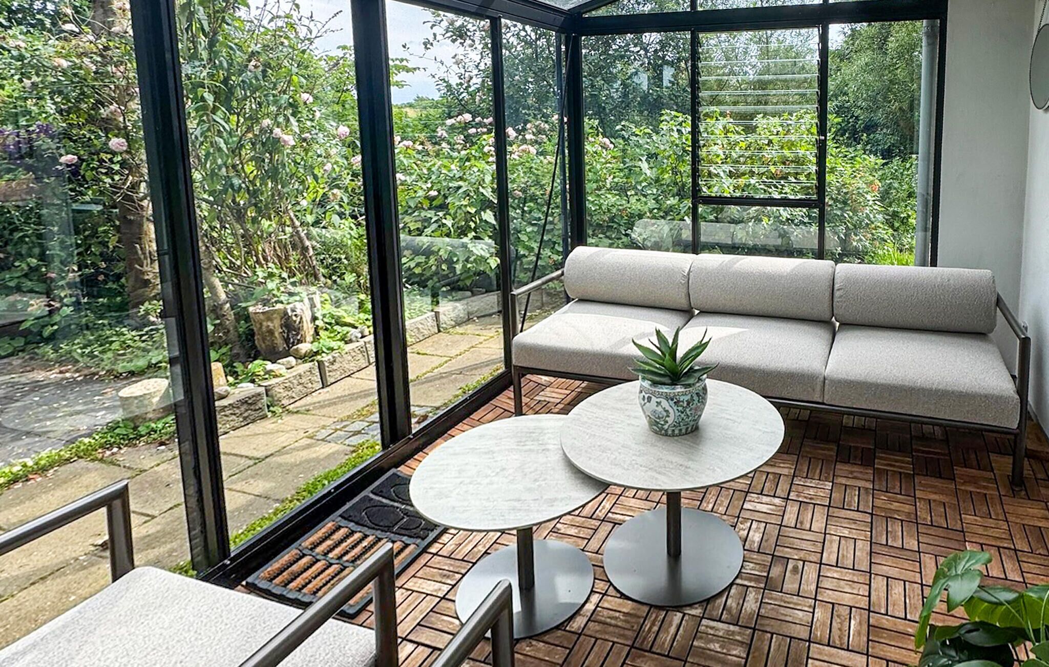A conservatory with a sofa, a table, and a potted plant.