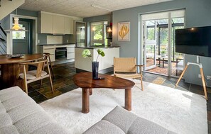 Een moderne keuken met witte kasten, een eethoek met een houten tafel en stoelen, een woonkamer met een bank en een televisie op een meubel.'
